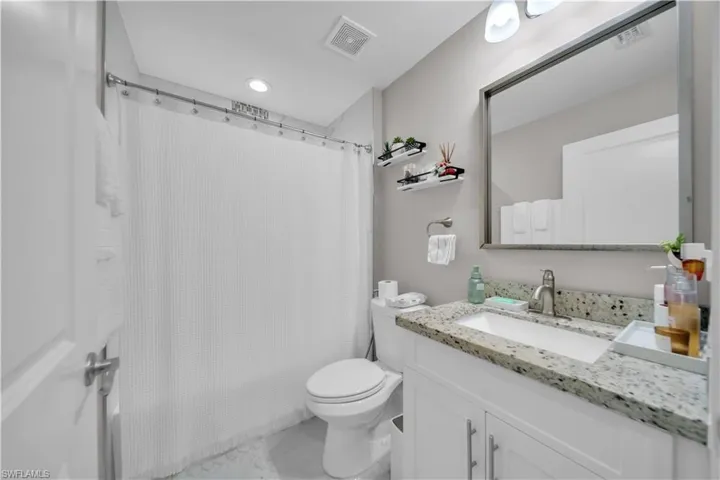 Contemporary bathroom featuring a white vanity with slab doors, granite countertop, undermount sink, and a framed mirror