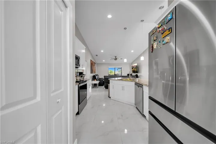 Open-concept kitchen featuring white cabinetry, stone-finish countertops, stainless steel appliances, and large-format tile flooring