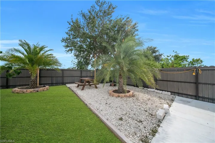 Expansive backyard featuring a manicured lawn, established palm trees with decorative stone surrounds, and a gravel-covered entertainment area
