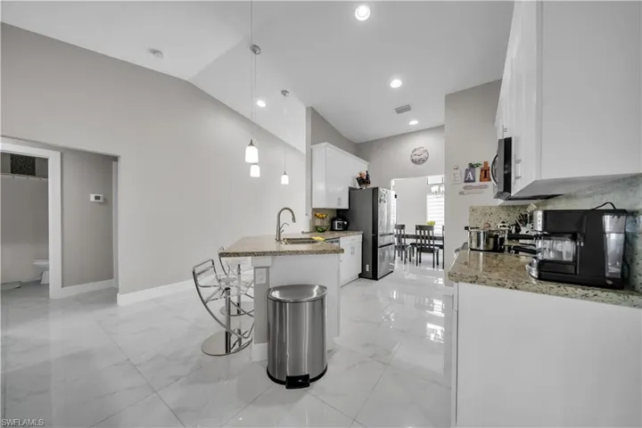 Modern kitchen featuring white cabinetry, granite countertops, an island with pendant lighting, a stainless steel refrigerator, and large format polished tile flooring