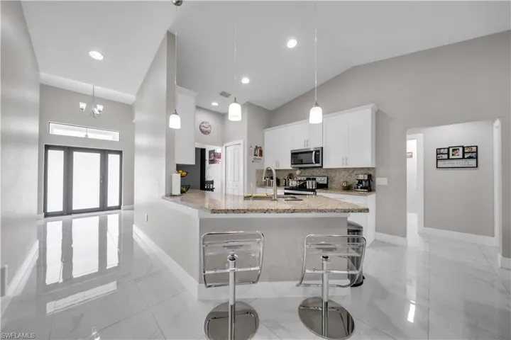 Gourmet kitchen featuring a peninsula with integrated seating, stone countertops, white cabinetry, and stainless steel appliances