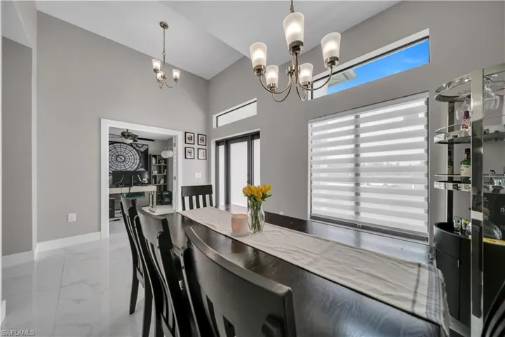 Vaulted ceiling featuring a contemporary chandelier, transom windows, large window with horizontal blinds, and white tile flooring