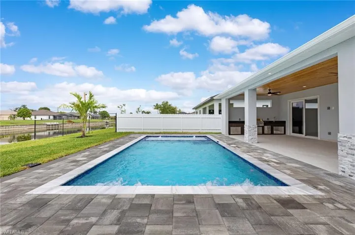 View of swimming pool with exterior kitchen, a patio area, a ceiling fan, and a water view