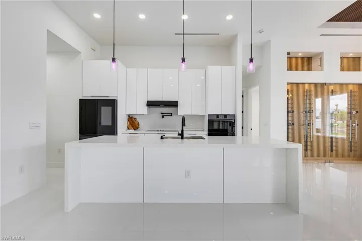 Kitchen with white cabinetry, hanging light fixtures, light stone counters, backsplash, and a spacious island