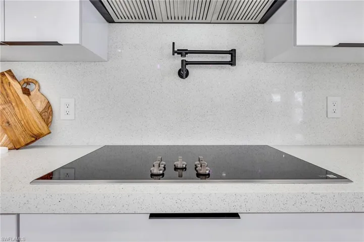 Kitchen view of black electric cooktop, ventilation hood, and tasteful backsplash
