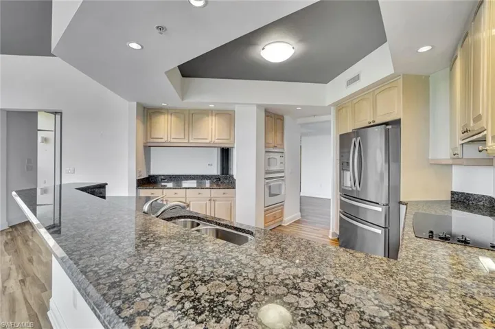 Kitchen with light wood-type flooring, white appliances, dark stone counters, a peninsula, and recessed lighting
