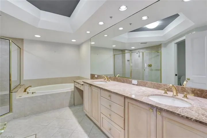 Bathroom with a tray ceiling, a stall shower, a garden tub, double vanity, and light tile patterned floors