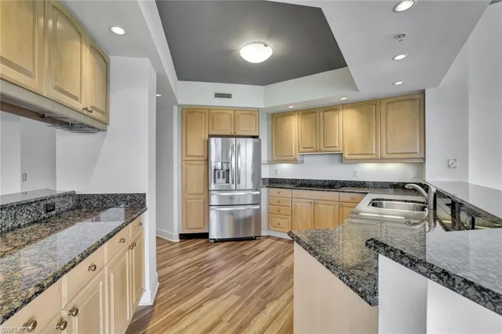 Kitchen featuring recessed lighting, stainless steel fridge with ice dispenser, dark stone countertops, light wood-style floors, and a raised ceiling