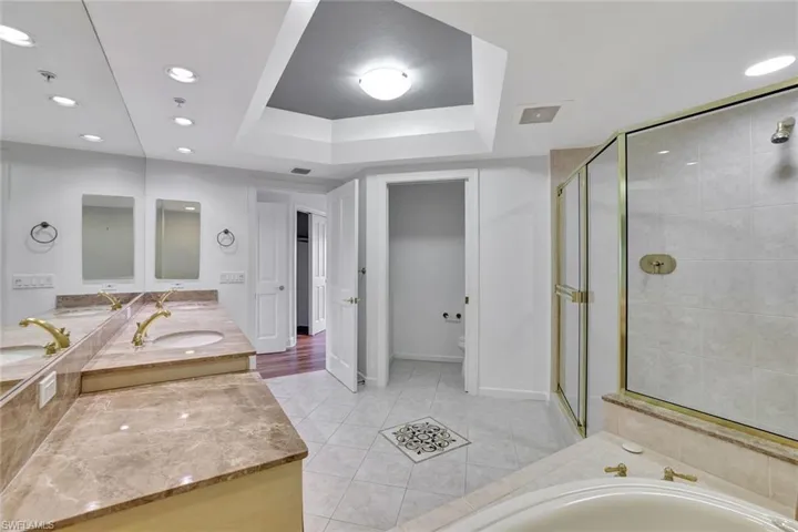 Full bath featuring recessed lighting, double vanity, a shower stall, light tile patterned floors, and a tray ceiling