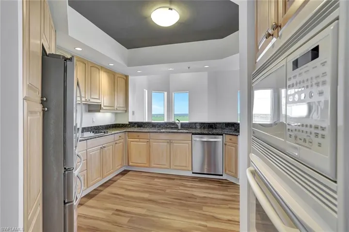 Kitchen with stainless steel appliances, light wood-type flooring, light brown cabinetry, dark stone counters, and recessed lighting
