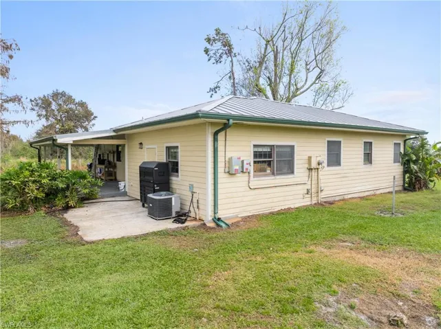 Back of house with a lawn, cooling unit, and a carport