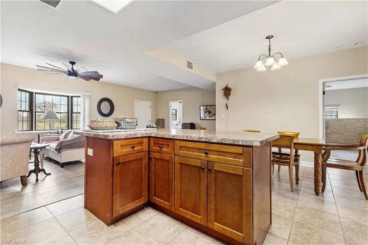 Kitchen with light tile patterned flooring, a kitchen island, pendant lighting, and ceiling fan with notable chandelier