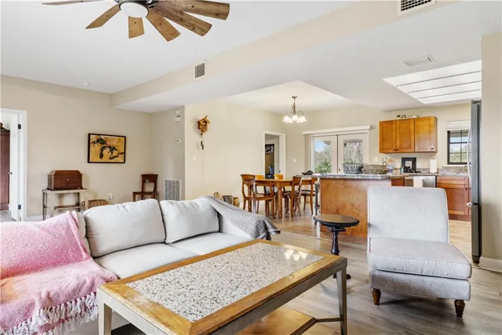 Living room with ceiling fan with notable chandelier, light wood-type flooring, and plenty of natural light