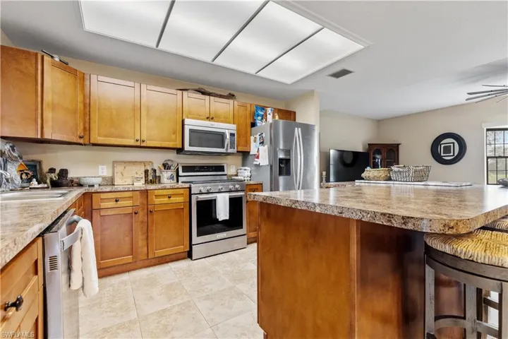 Kitchen featuring sink, ceiling fan, light tile patterned floors, appliances with stainless steel finishes, and a kitchen bar