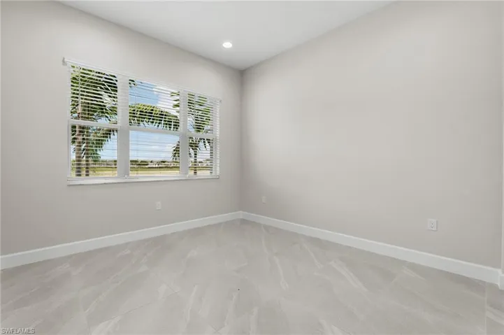 Guest bedroom with large window with white blinds, recessed lighting, light gray walls, white baseboards, and gray marble-look tile flooring
