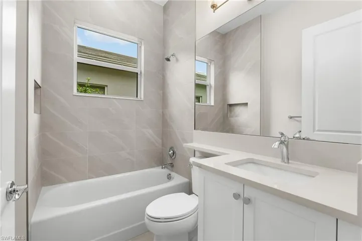 Full bathroom featuring a single vanity with an integrated sink, a large mirror, a built-in bathtub with shower, and light-toned wall tiling