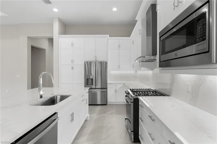 Modern kitchen featuring white cabinetry, light-premium quartz countertops & backsplash, and stainless steel appliances with vented hood.