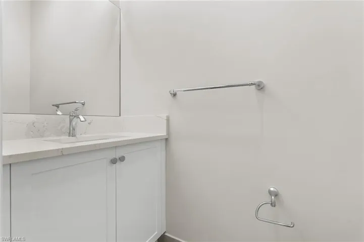 Guest powder room vanity featuring a quartz countertop with an integrated sink, polished chrome faucet, and white Shaker-style cabinetry with circular hardware