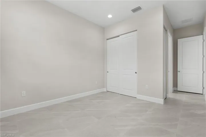 Spacious room featuring light gray walls, large format tile flooring, white baseboards, a double sliding closet door, and recessed lighting