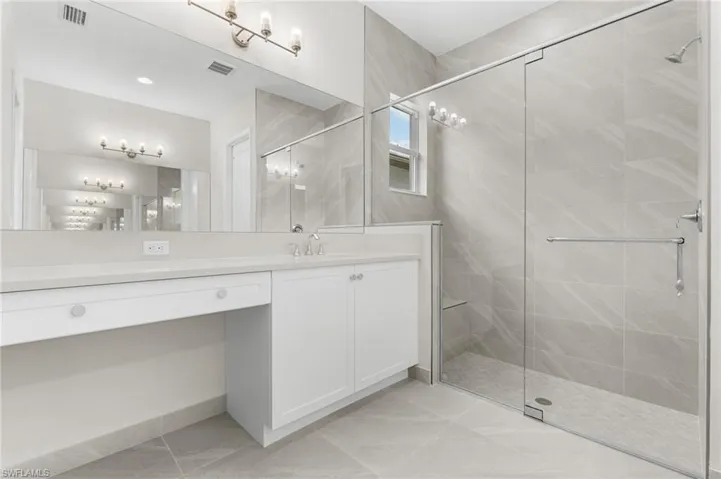 Primary bathroom featuring dual vanities with white cabinetry, quartz countertop, a large mirror, tile-to ceiling shower with seamless shower enclosure with 3/8" glass.