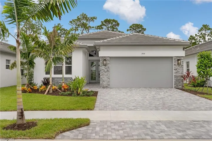Contemporary home exterior featuring a tile roof, stacked stone accents, paver driveway, and a landscaped entry with palm trees