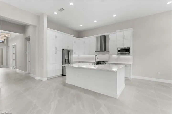 Modern kitchen featuring a central island, white shaker-style cabinetry, stainless steel appliances and vented hood, recessed lighting, premium quartz counters and backsplash.