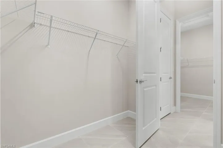 2 master walk-in closets featuring wire shelving, white baseboards, and light-toned tile flooring