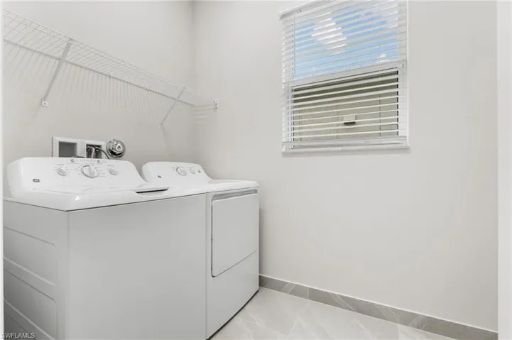 Laundry area featuring a window with blinds, a white wire shelving unit, and tile flooring with matching base trim