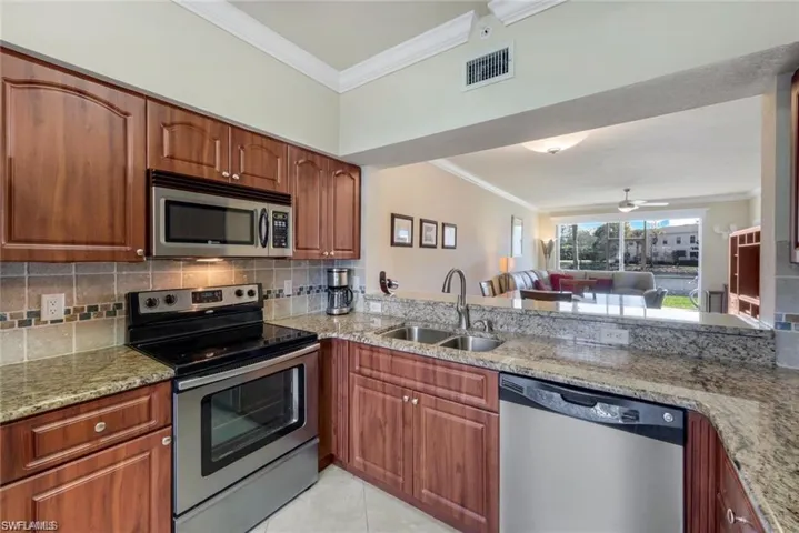 Kitchen with stainless steel appliances, decorative backsplash, crown molding, open floor plan, and light stone counters