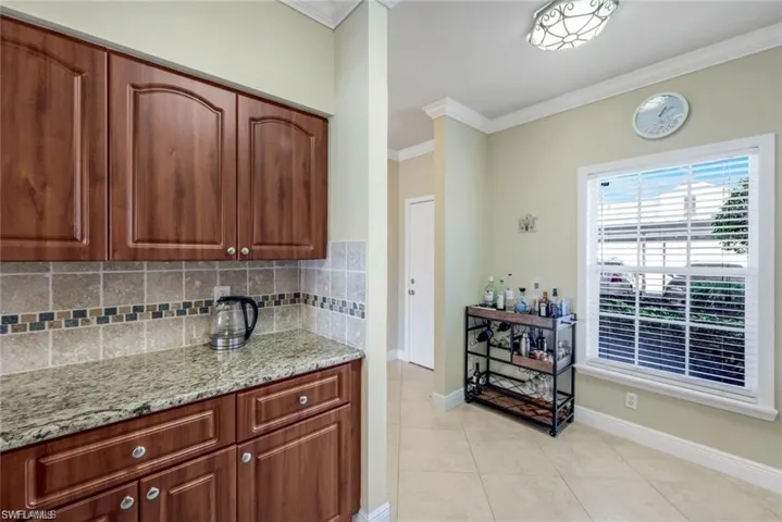 Kitchen featuring ornamental molding, light stone counters, decorative backsplash, light tile patterned floors, and brown cabinetry