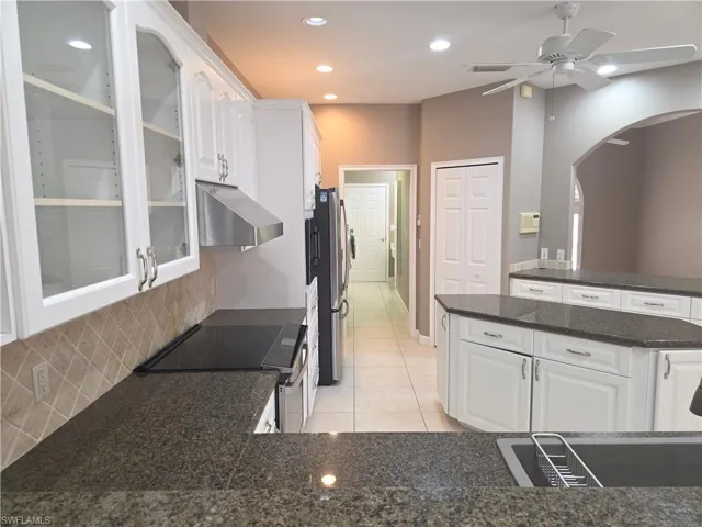 Kitchen featuring stainless steel appliances, arched walkways, light tile patterned floors, white cabinets, and recessed lighting