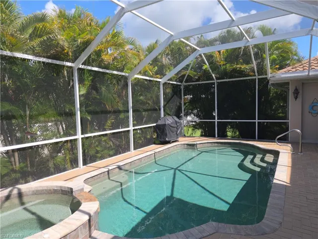 View of swimming pool with glass enclosure, grilling area, and a pool with connected hot tub