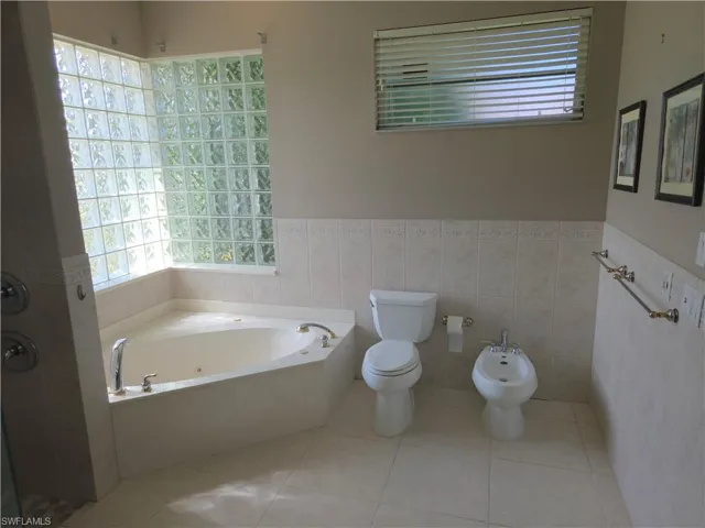 Bathroom featuring a jetted tub, wainscoting, tile walls, tile patterned floors, and a bidet
