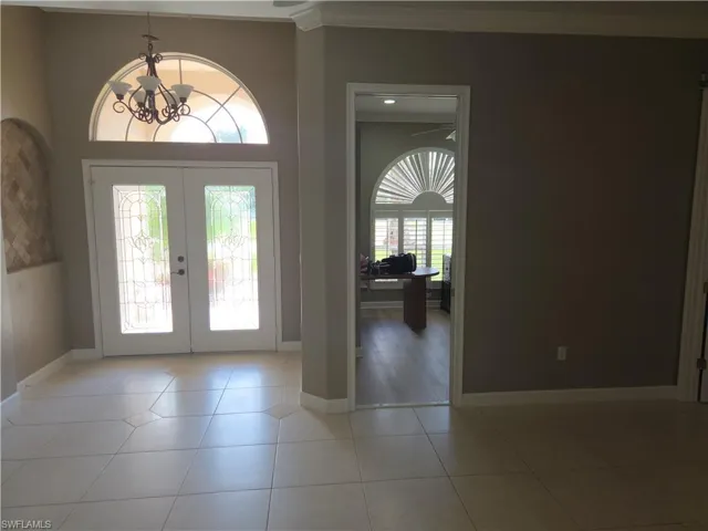 Foyer featuring french doors, a chandelier, light tile patterned floors, and ornamental molding
