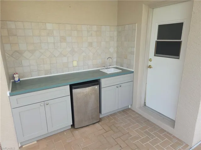 Kitchen featuring dishwashing machine, decorative backsplash, brick patterned floors, and white cabinetry