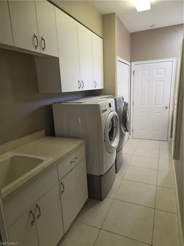 Washroom with washing machine and clothes dryer, cabinet space, and light tile patterned flooring
