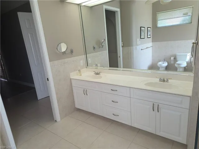Full bath featuring tile walls, a wainscoted wall, tile patterned floors, a bidet, and double vanity