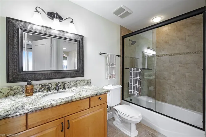 Full bathroom featuring tile patterned floors, bath / shower combo with glass door, toilet, and vanity