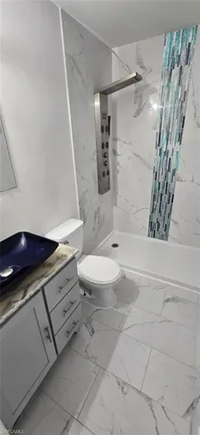 Full bathroom with vanity, a marble finish shower, and light marble finish floors