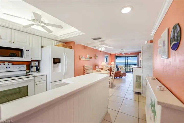 Kitchen with light tile patterned floors, white appliances, ceiling fan, white cabinetry, and kitchen peninsula