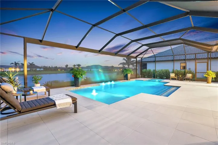 Pool at dusk featuring a patio, glass enclosure, and a water view