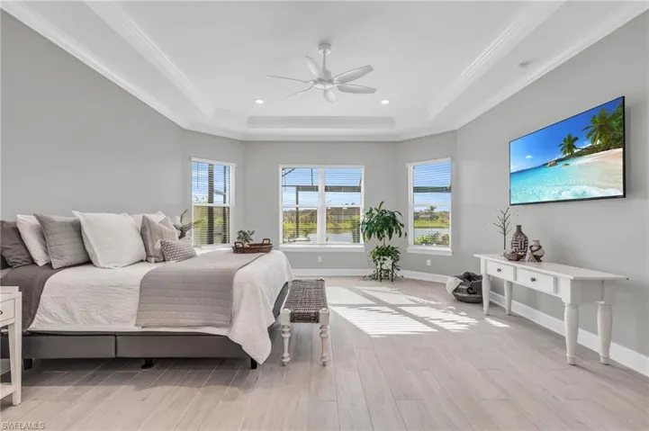 Bedroom with ceiling fan, light hardwood / wood-style flooring, crown molding, and a tray ceiling