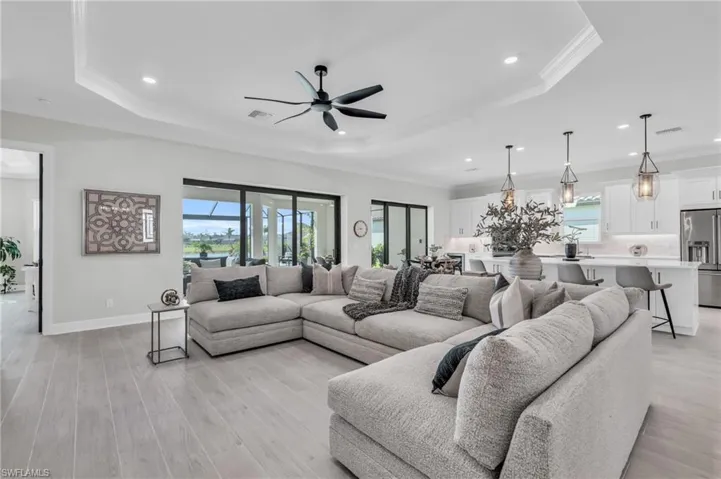 Living room with ceiling fan, a tray ceiling, crown molding, and light hardwood / wood-style floors
