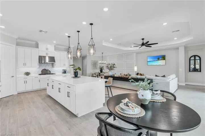 Kitchen featuring ceiling fan, hanging light fixtures, a kitchen island, white cabinetry, and a tray ceiling
