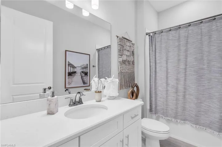 Full bathroom featuring hardwood / wood-style floors, shower / tub combo with curtain, vanity, and toilet