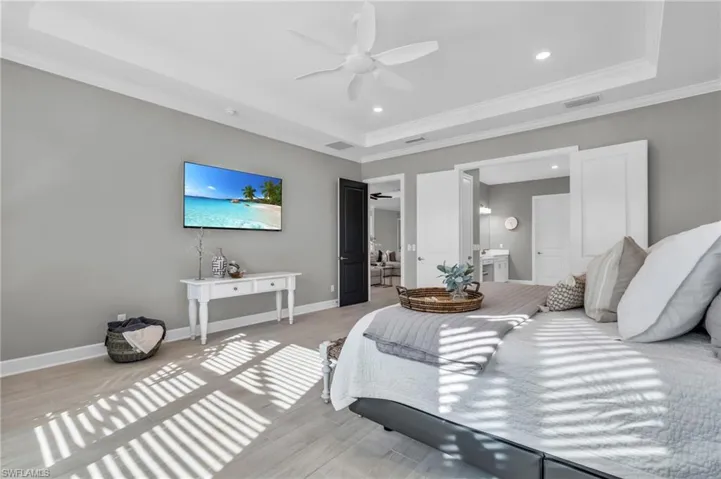 Bedroom featuring light wood-type flooring, connected bathroom, a tray ceiling, and ceiling fan