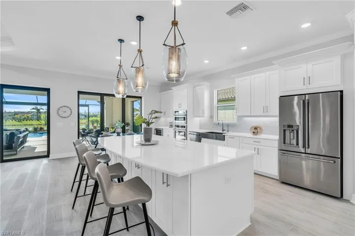 Kitchen with light hardwood / wood-style floors, a center island, white cabinetry, appliances with stainless steel finishes, and decorative light fixtures