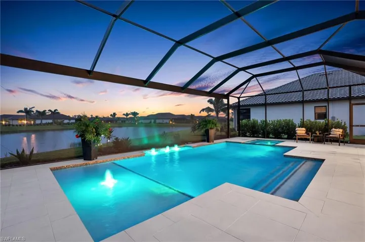 Pool at dusk featuring a patio, a water view, and glass enclosure
