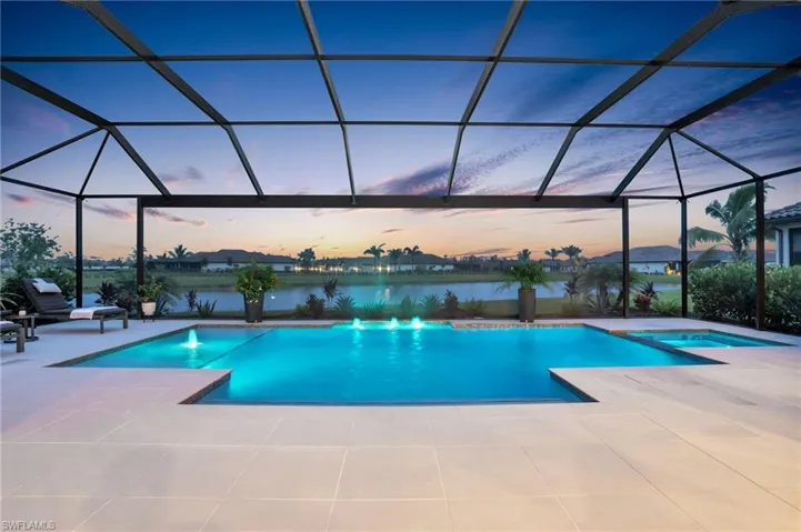 Pool at dusk with a patio, glass enclosure, a water view, and a hot tub