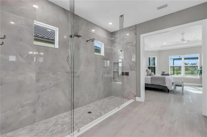 Bathroom featuring a tile shower, a tray ceiling, ceiling fan, and hardwood / wood-style flooring